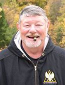 Man with grey beard smoking a cigar, wearing a heavy black jacket